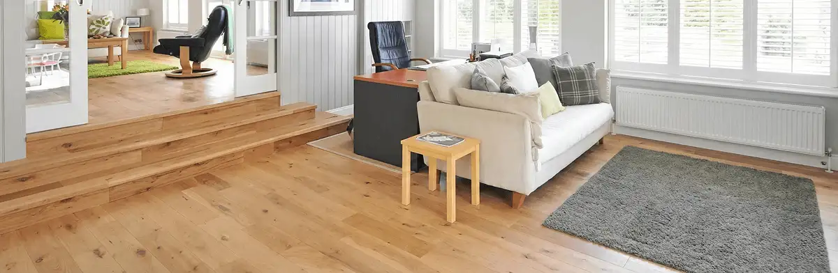 A modern living room with professionally installed laminate flooring, a beige sofa, a small side table, a gray rug, and large windows with white shutters in Pembroke Pines, FL
